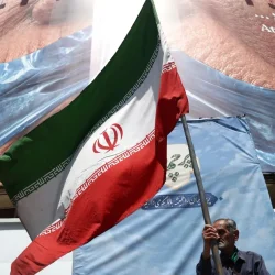 Homem-segura-bandeira-iraniana-perto-de-outdoor-anti-EUA-representando-o-presidente-dos-EUA-Donald-T.webp