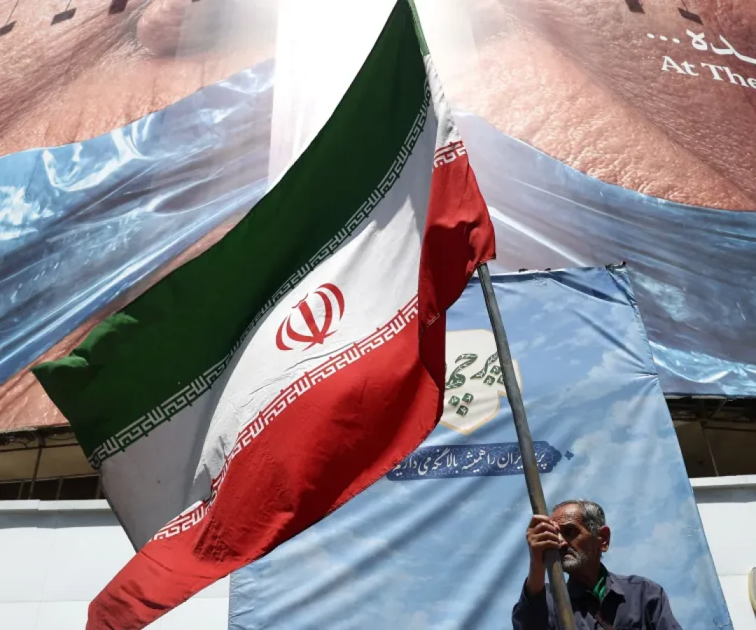 Homem-segura-bandeira-iraniana-perto-de-outdoor-anti-EUA-representando-o-presidente-dos-EUA-Donald-T.webp