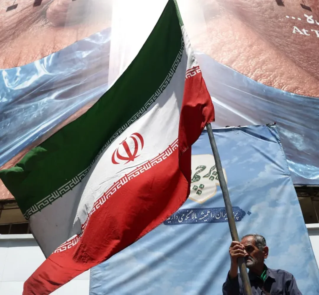 Homem-segura-bandeira-iraniana-perto-de-outdoor-anti-EUA-representando-o-presidente-dos-EUA-Donald-T.webp